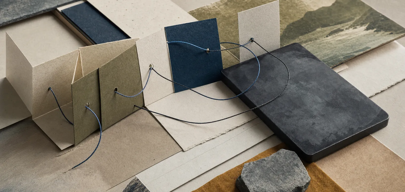 An editorial still life suggesting data integration and systems work: layered paper panels and fine threads on a warm desk